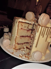 Cargar imagen en el visor de la galería, Pastel de vainilla con betún de mantequilla relleno de limón y mermelada. Decoración con macarons, perlas de color plateado comestibles, un drip de oro comestible y un topper de cumpleaños.
