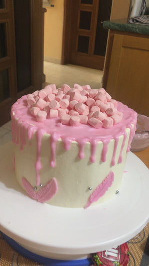 Video del pastel de vainilla cubierto de betún de mantequilla color rosa con bombones rosas y plumas de chocolate blanco. 