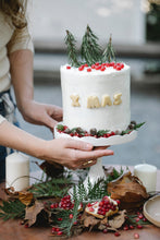 Cargar imagen en el visor de la galería, Pastel red velvet con betún de mantequilla y azúcar glass para 10 personas. La decoración incluye granada, galletas de mantequilla para las letras "X MAS" y mini pinitos navideños y piñitas de pino artificiales.
